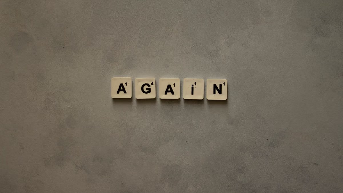 Close-up of Scrabble tiles spelling out 'Again' on a textured background.